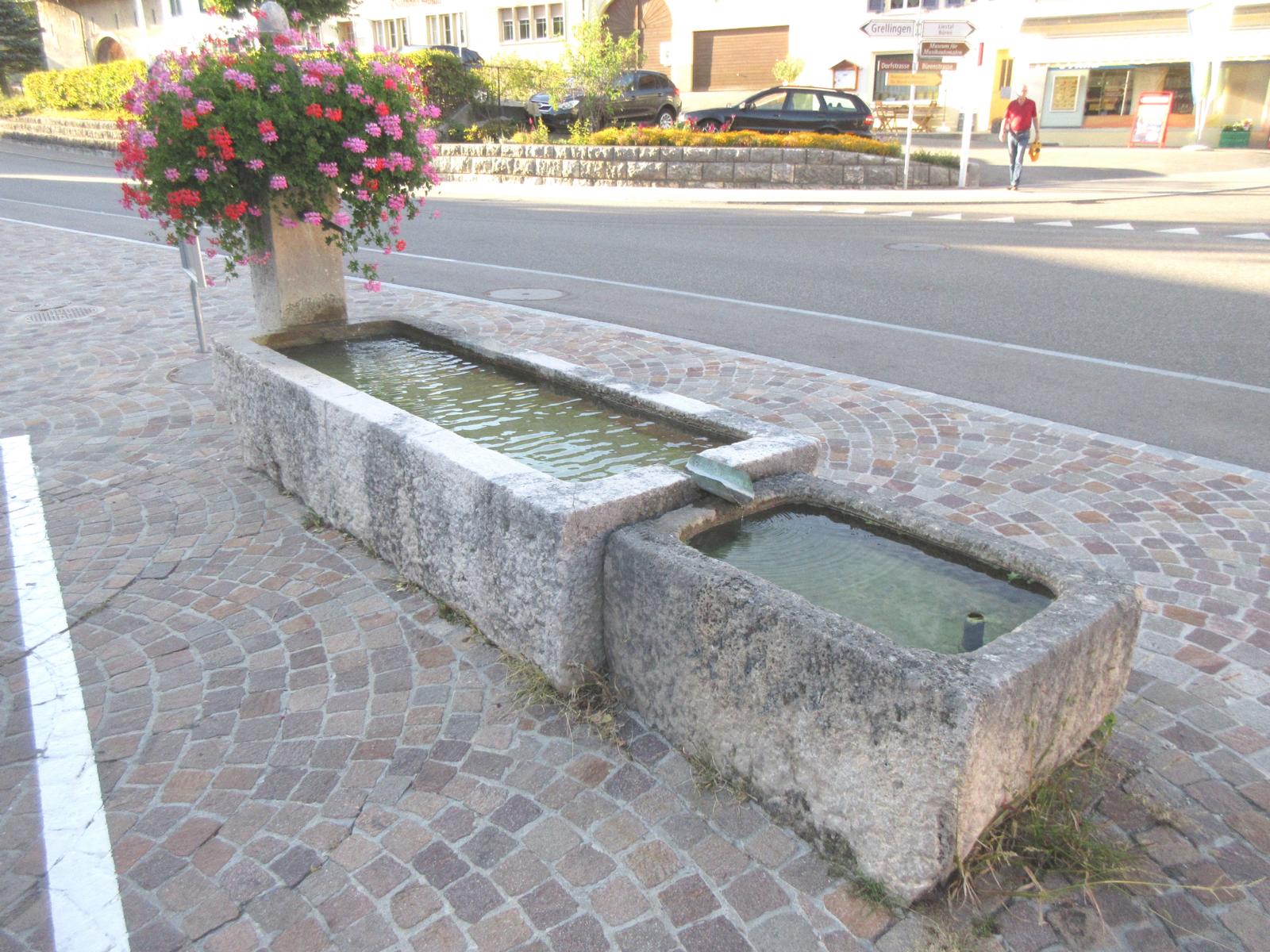 Dorfstrasse *** 2003 (datiert Metallgestell für Blumen) *** Laufener Kalkstein (Monolith 2.7 x 1.0 m) *** Laufener Kalkstein *** Wasser von lokaler Quelle ("Kein Trinkwasser")
